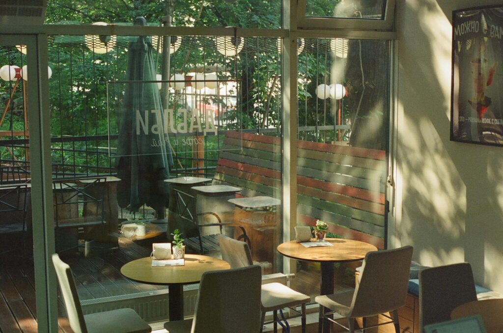 A serene indoor café setting featuring stylish chairs and tables bathed in sunlight through large glass windows.